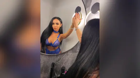 Glamorous woman with long black hair in a blue mesh bikini posing in a modern marble bathroom mirror.