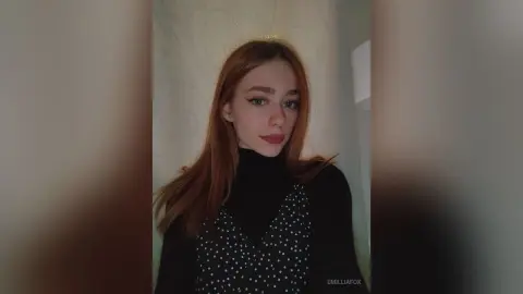 Redheaded woman in a black turtleneck and polka dot top posing with a moody expression indoors.