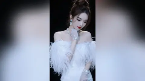 Elegant woman in a white feathered off-the-shoulder gown and silver gloves posing glamorously.