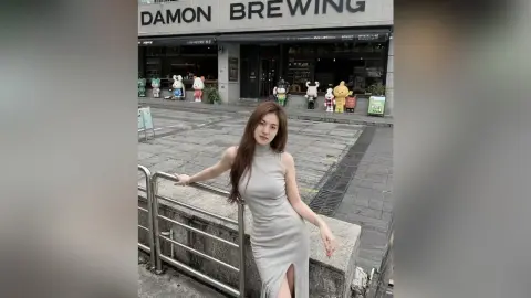 Young woman in a grey sleeveless dress leaning on a railing outside Damon Brewing cafe on a sunny day.
