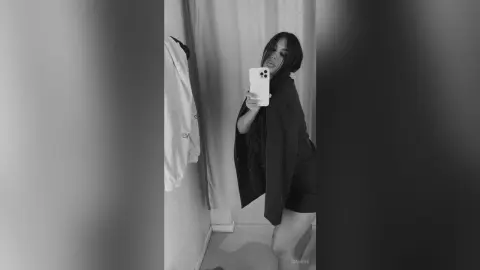 Young woman in a black oversized sweater taking a moody black and white mirror selfie indoors.