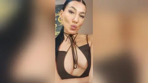 Young woman in a brown halter neck cutout top making a playful kissy face in a cozy indoor setting.