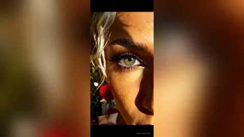 Close-up portrait of a blonde woman with striking green eyes and natural makeup in warm sunlight.