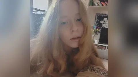 Blonde woman with freckles in a cozy indoor setting looking thoughtfully at the camera.