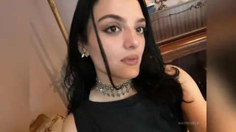 Young woman with long dark hair wearing a silver charm choker necklace in a warm indoor setting.