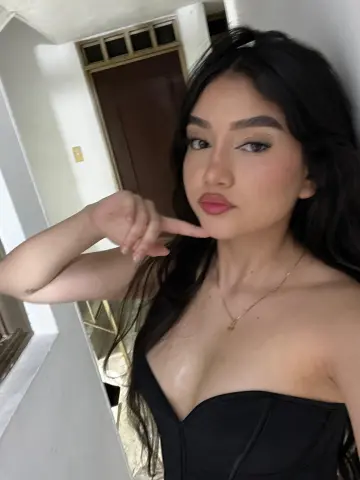 Young woman in a black corset top posing indoors with a confident expression.