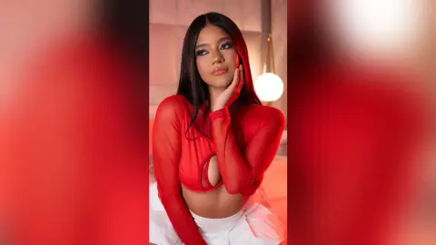 Young woman in a red long-sleeve crop top posing elegantly in a warm, dimly lit indoor setting.