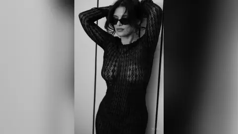 Elegant woman in a black lace long-sleeve dress and sunglasses posing in a moody black and white portrait.