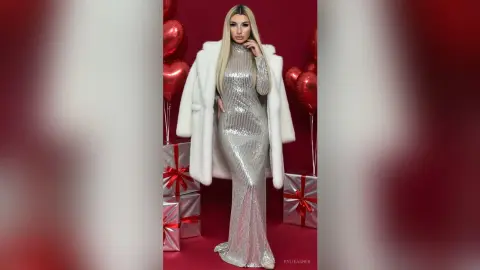 Glamorous blonde woman in a silver sequin gown and white faux fur coat posing with red balloons and gift boxes.