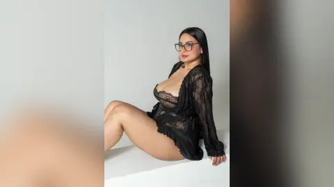 Curvy woman in black lace lingerie and sheer robe posing confidently against a white studio background.