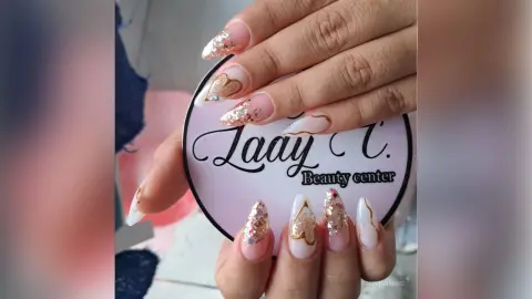 Close-up of elegant nude manicure with gold glitter and heart nail art designs for a romantic beauty look.