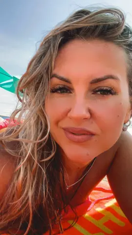 Smiling blonde woman in summer beachwear relaxing on a bright orange towel under the sun.