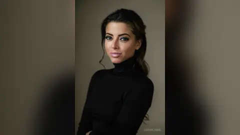 Elegant woman in a black turtleneck sweater posing with a sophisticated and moody expression against a neutral background.