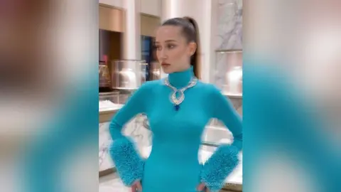 Elegant woman in a turquoise turtleneck dress and statement silver necklace posing in a luxury jewelry store.