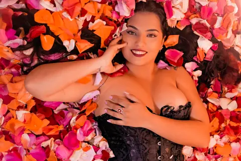 Smiling woman in black lace lingerie lying on a bed of vibrant pink and orange rose petals.