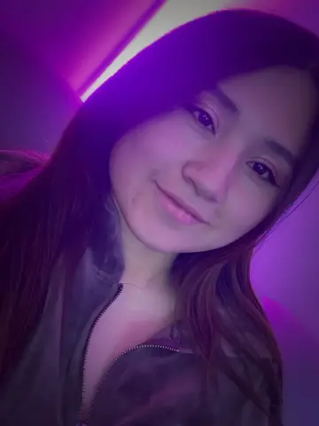 MiaHarveyyy smiles while wearing a dark zip-up jacket under purple neon lighting.