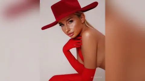 Glamorous woman in a red wide-brimmed hat and matching gloves posing against a minimalist studio background.