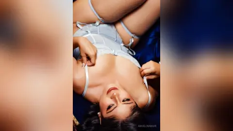 Glamorous woman in elegant white lace lingerie relaxing on blue fabric in a moody, intimate setting.