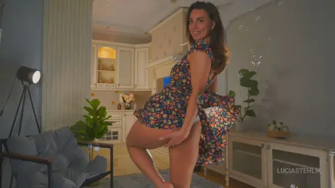 Smiling woman in a floral summer dress posing in a bright, modern living room.