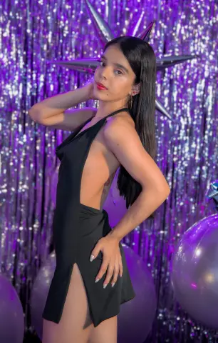 Young woman in a sleek black cutout dress posing against a shimmering purple party backdrop.