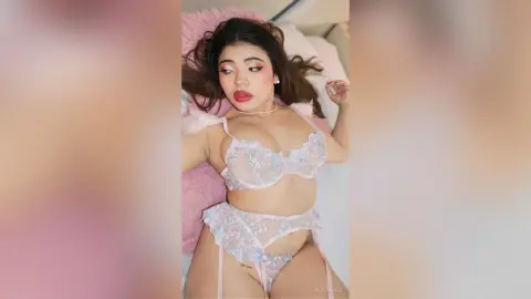 Young woman in lace pink lingerie lying on a bed with a dreamy, romantic mood.
