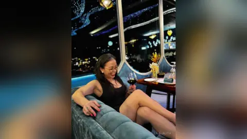 Smiling woman in a black dress enjoying red wine on a luxury rooftop lounge at night.