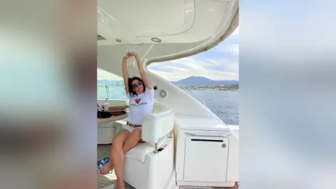 Relaxed woman in white t-shirt and sunglasses lounging on a luxury yacht deck overlooking the blue ocean.