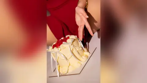 RebecaVillalobos reaches a hand toward a white frosted cake topped with red berries.