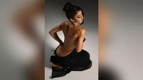 Elegant woman in a black backless dress posing gracefully against a minimalist studio background.