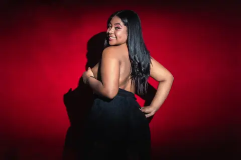Smiling Black woman in a black backless dress posing against a dramatic red background.