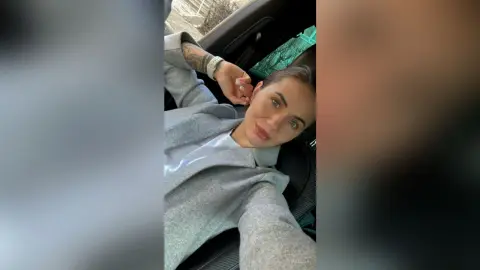 Young woman in a grey sweatshirt relaxing inside a car with a casual, serene mood.