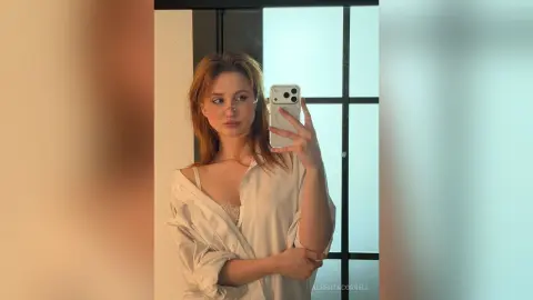AlbertaCorrell takes a mirror selfie wearing a loose, open white shirt and lace lingerie.