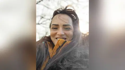 Smiling woman in a cozy brown faux fur coat enjoying a sunny outdoor day in nature.