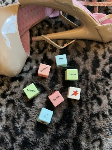 Small colorful dice with intimate words scattered on a dark faux fur rug next to beige high heel pumps.