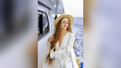 Smiling woman in a white linen dress and straw hat relaxing on a boat in the sunny ocean.