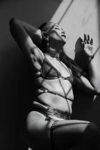Moody black and white portrait of a woman in minimalist lingerie posing in dramatic sunlight shadows.