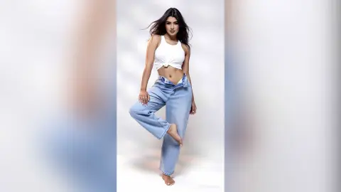 MarianSajir poses in a white crop top and unbuttoned blue jeans, showing her belly and midriff.