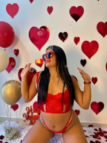 Smiling woman in red lace lingerie posing against a romantic heart backdrop for Valentine's Day.