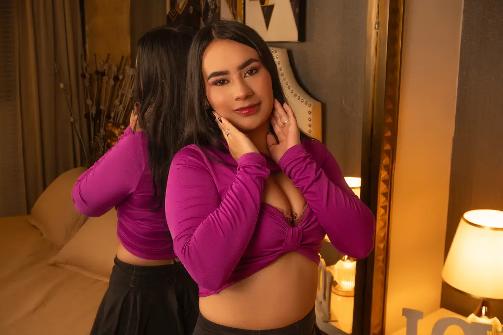 MadelynWalkerG — Young woman in a purple long-sleeve crop top posing in a warm, cozy bedroom setting.