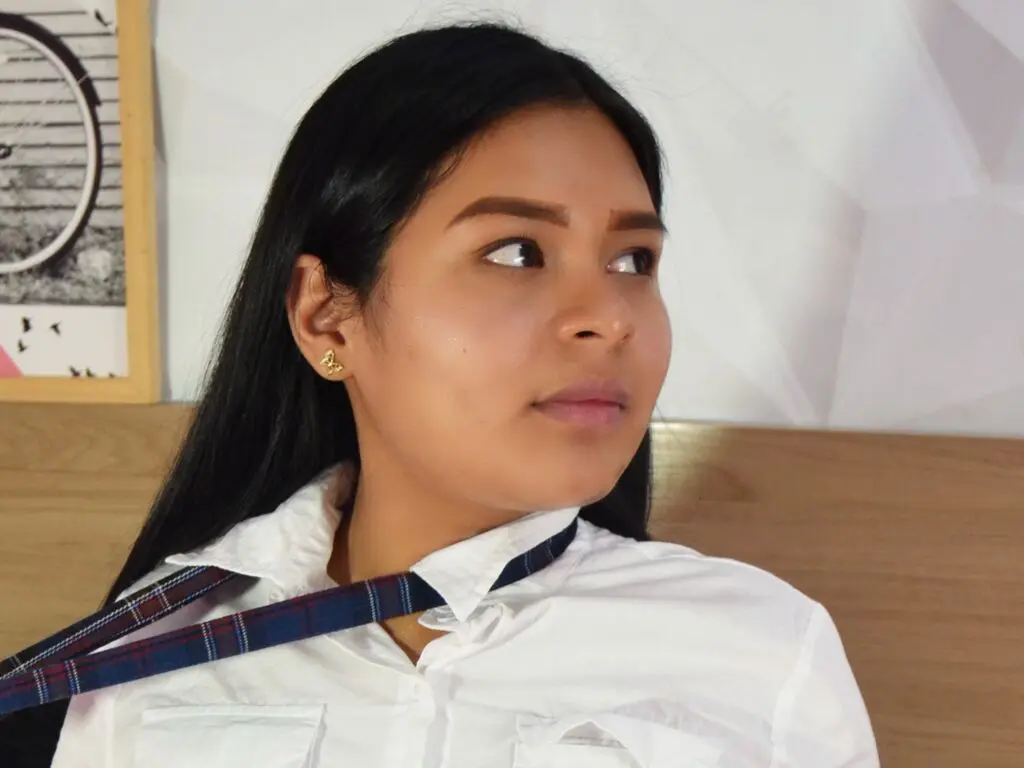 Young woman in a white button-down shirt and plaid tie looking thoughtfully in a bright indoor setting.
