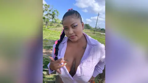 Young woman in a white button-down shirt posing outdoors in a sunny green field with a confident expression.