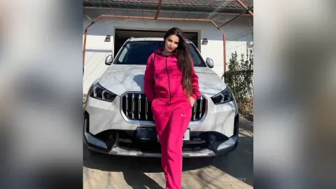 Stylish woman in a pink tracksuit posing confidently in front of a white luxury SUV outdoors.