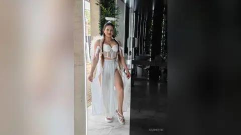 Woman in white angel costume with wings and halo posing in a modern minimalist room.