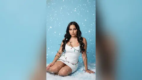 Beautiful woman in a white dress sitting in artificial snow against a blue background for a festive winter shoot.