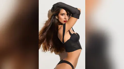 Glamorous woman in black lingerie and long gloves posing against a white background with a moody aesthetic.