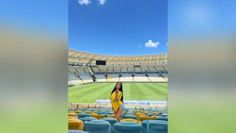 Young woman in a yellow jersey sitting in stadium seats under a clear blue sky.