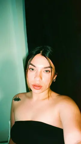 Young woman with dark hair in a black strapless top posing for a moody indoor selfie.