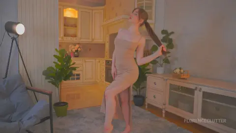 Elegant woman in a beige midi dress posing in a warm, cozy modern kitchen setting.