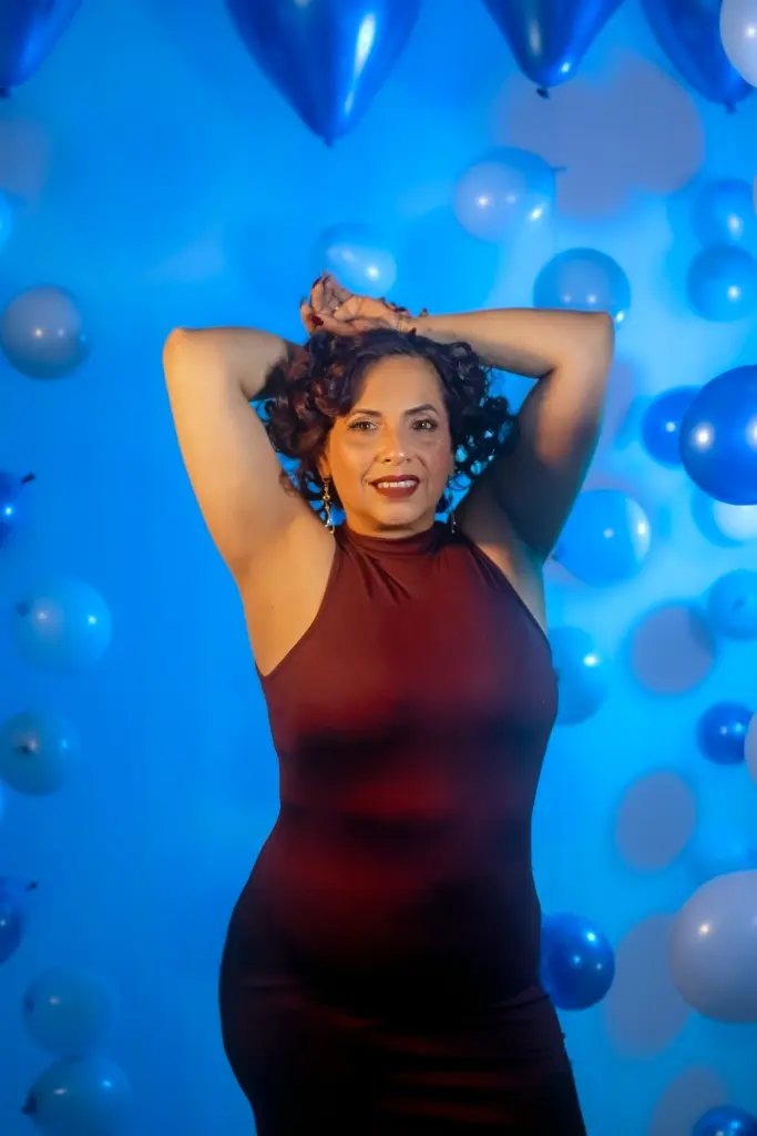 GochitaWild smiles while touching her face, wearing a black tube top and orange patterned bottoms against a white curtain backdrop.