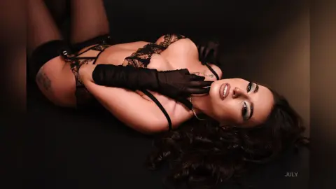 Glamorous woman in black lace lingerie and long gloves lying on a dark background with a moody aesthetic.